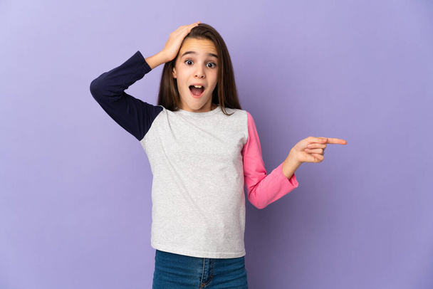 Little girl isolated on purple background surprised and pointing finger to the side - Photo, Image