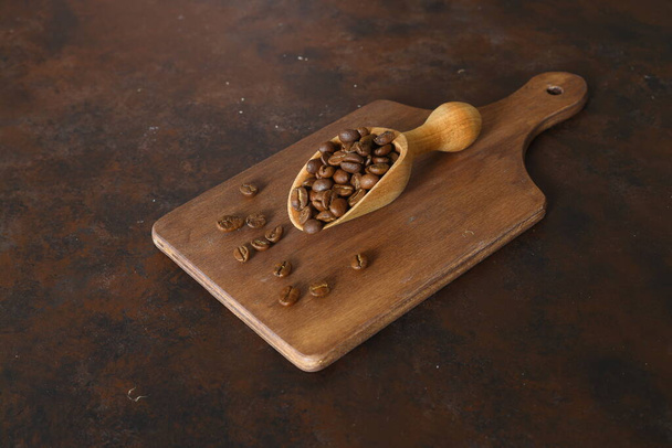 Granos de café en una cucharada de madera aislada sobre un fondo oscuro. Granos de café tostados aislados. Una cucharada de madera con café. - Foto, imagen