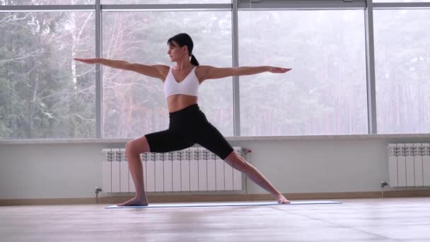 Молодая женщина йога, практикующая йогу, стоящая во втором упражнении Воина, - Кадры, видео