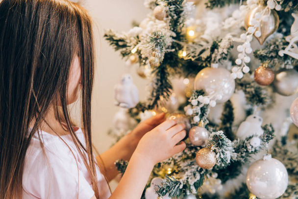 Adorable little girl decorating a Christmas tree with baubles at home - Фото, зображення