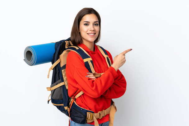 Young caucasian mountaineer girl with a big backpack isolated on white background pointing finger to the side - Photo, Image
