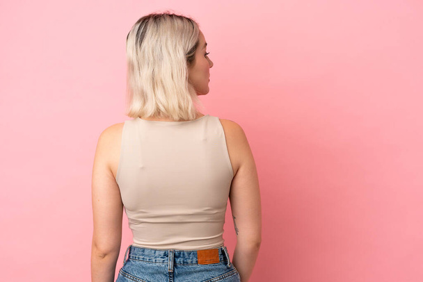 Young caucasian woman isolated on pink background in back position and looking side - Foto, Imagen
