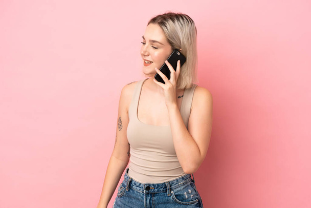 Junge kaukasische Frau isoliert auf rosa Hintergrund hält ein Gespräch mit dem Handy mit jemandem - Foto, Bild