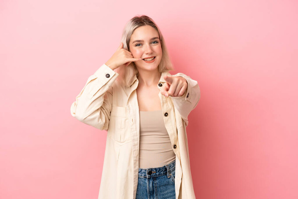 Young caucasian woman isolated on pink background making phone gesture and pointing front - Foto, imagen