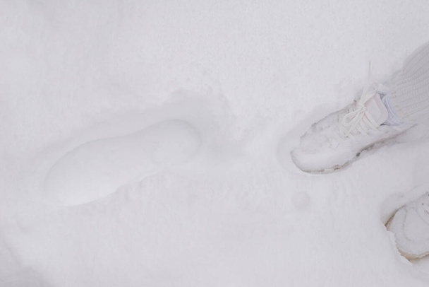 Žena v bílých kalhotách a bílých teniskách stojí ve sněhu.  - Fotografie, Obrázek