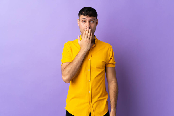 Young Colombian man isolated on purple background covering mouth with hand - Foto, Imagem