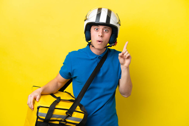 Young Brazilian man with thermal backpack isolated on yellow background intending to realizes the solution while lifting a finger up - 写真・画像