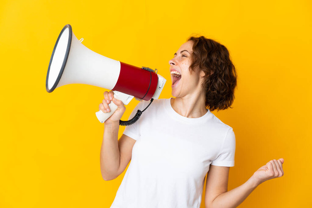 Young English woman isolated on yellow background shouting through a megaphone to announce something in lateral position - Photo, Image