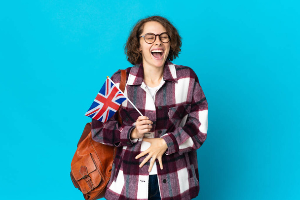 Joven mujer inglesa sosteniendo una bandera del Reino Unido aislada sobre fondo azul sonriendo mucho - Foto, imagen