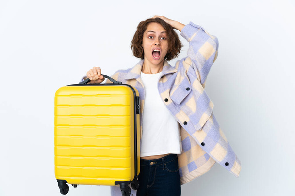 Young English woman isolated on white background in vacation with travel suitcase and surprised - Photo, Image