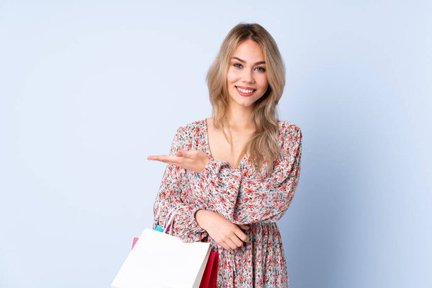 Teenager russische Mädchen mit Einkaufstasche isoliert auf blauem Hintergrund präsentiert eine Idee, während lächelnd in Richtung - Foto, Bild