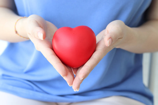 Close-up van de vrouw hand met rood hart op blauwe shirt achtergrond. Gezondheid, geneeskunde en liefdadigheid  - Foto, afbeelding