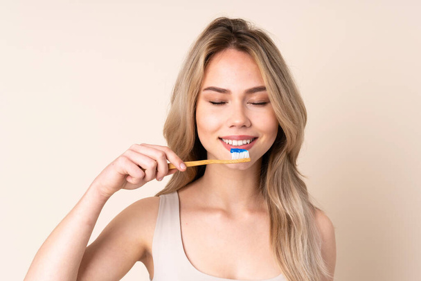 Teenager blonde girl brushing her teeth over isolated background - Фото, изображение