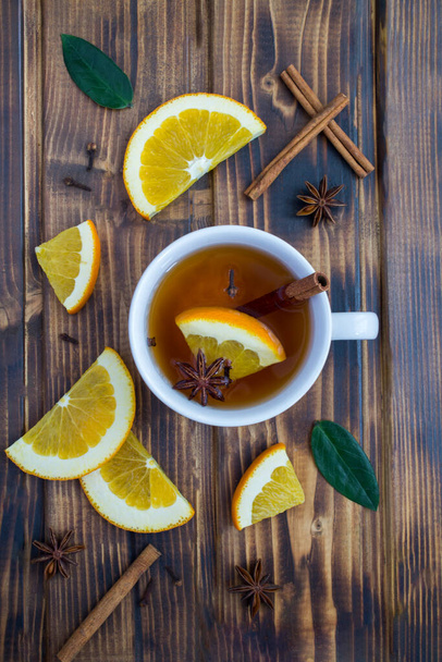 Vista superior del té con naranja, canela y anís en la taza blanca sobre el fondo de madera. Primer plano. - Foto, Imagen