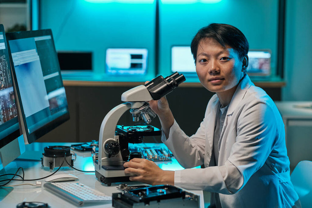 Jonge Aziatische onderzoeker in whitecoat werken met microscoop - Foto, afbeelding