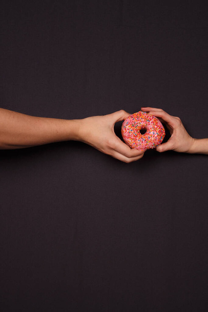 Typisch amerikanische Süßigkeiten - Donuts in der Hand auf dunklem Hintergrund - Foto, Bild