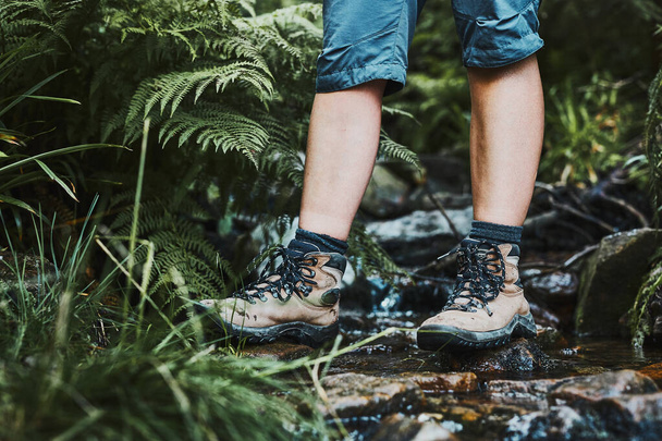 Female legs with trekking boots standing on stones in mountain stream. Summer vacation close to nature. Concept of actively spending leisure time - Фото, зображення