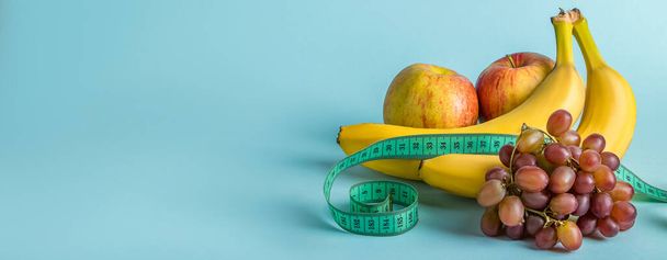 Measuring tape and juicy fruits on a blue background. The concept of diet and proper nutrition. Banner format, place for text. - Photo, Image