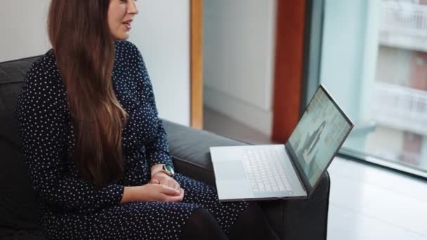 Mujer joven sentada en el sofá en casa conversando con el terapeuta virtual en el portátil - Imágenes, Vídeo