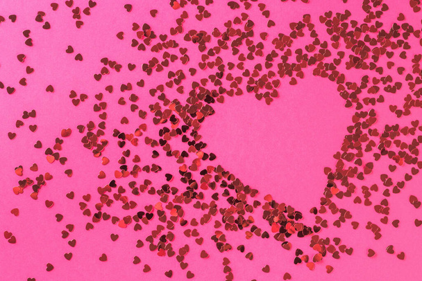 Un cuore creativo fatto di un gran numero di piccoli cuori lucenti su uno sfondo rosa. Il concetto di San Valentino. Posa piatta. - Foto, immagini