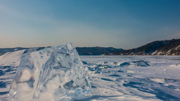 凍結した雪に覆われた湖の上には透明度の高い大きな氷の海が垂直に立っている。端に太陽がぎらつきます。澄んだ青い空に対する沿岸の山の範囲。コピースペース。バイカル - 写真・画像