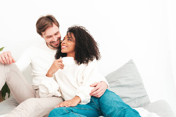 Smiling beautiful woman and her handsome boyfriend. Happy cheerful multiracial family having tender moments. Multiethnic models lying in bed and hugging in white interior. Embracing each other - Фото, изображение