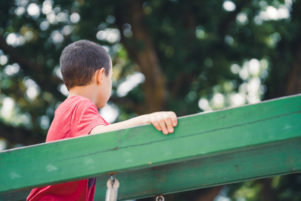 Niño con una camiseta roja corre a través de un puente de madera verde en el patio de recreo - Foto, imagen