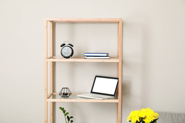 Wooden shelving unit with laptop and alarm clock near light wall - Photo, Image