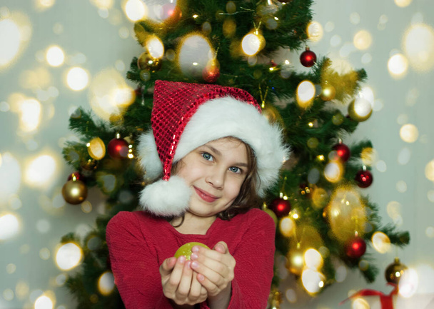 Portrait of a girl with a Christmas tree toy in her hands. A girl holds a golden Christmas ball in her hands - Foto, afbeelding