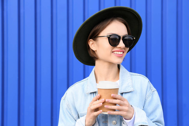 Fashionable smiling woman holding paper cup of tea on blue background - Foto, immagini