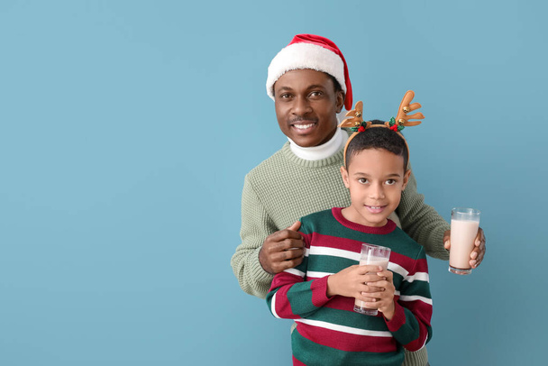 Niño afroamericano y su padre con decoración navideña y sabroso chocolate caliente sobre fondo de color - Foto, Imagen