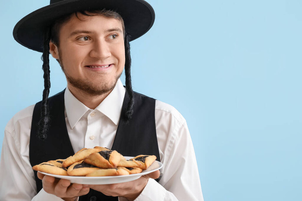 Young Jewish man with tasty Hamantaschen for Purim holiday on color background - Photo, Image