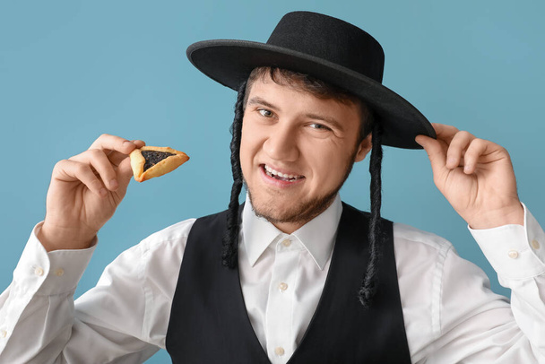 Mladý židovský muž s chutným Hamantaschen pro Purim dovolenou na šedém pozadí - Fotografie, Obrázek