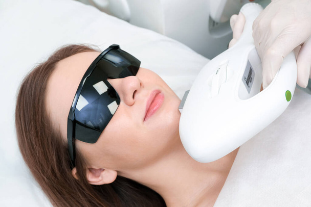 Laser hair removal of the mustache and chin of a young beautiful woman. Depilation on the face. Device for laser hair removal. - Photo, Image