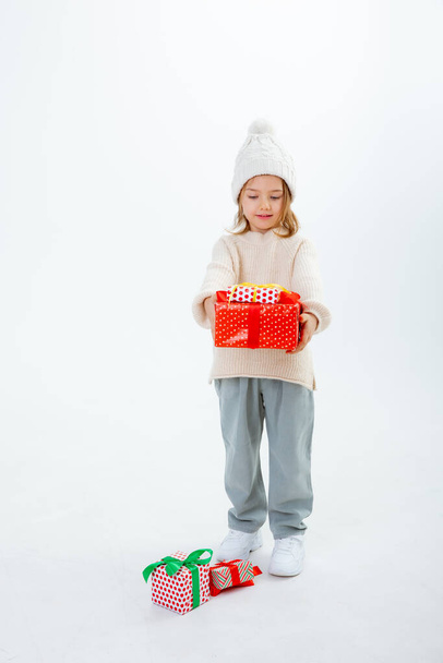 schattig klein kind in de winter hoed met dozen van geschenken geïsoleerd op een witte achtergrond - Foto, afbeelding