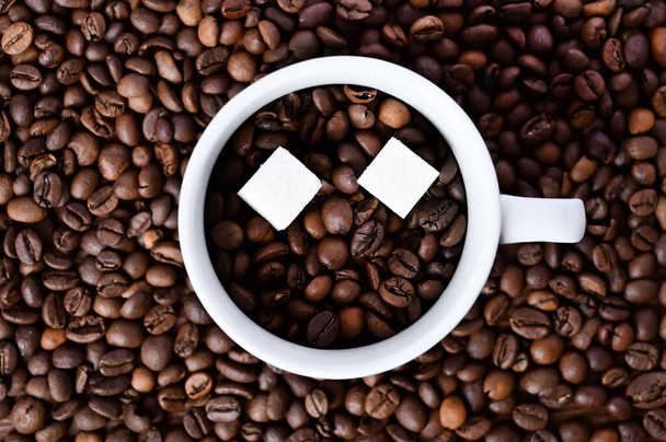 white cup with coffee beans and two pieces of sugar on a coffee background. Close-up. Flat layout with top view - Foto, immagini