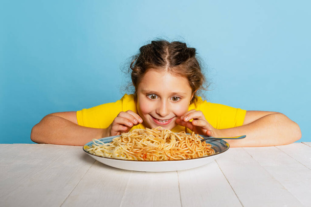 Cute little girl, emotive kid eating delicious Italian pasta isolated on blue studio background. World pasta day - Фото, зображення