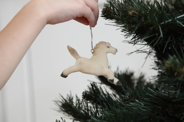 White children's hand hang a horse old toy on the Christmas tree closeup  - Foto, Imagem