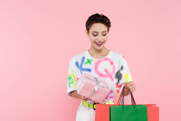 zadowolona brunetka kobieta z pudełka i torby na zakupy izolowane na różowy - Zdjęcie, obraz