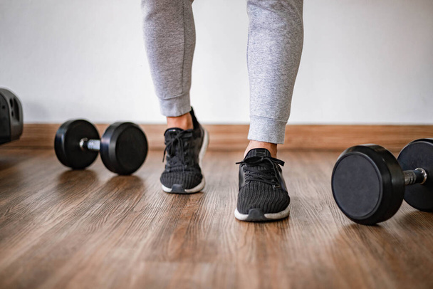 Training gym concept a lower body of a man wearing gray pants and black shoes standing on the floor with dumbbells. - Foto, Imagen