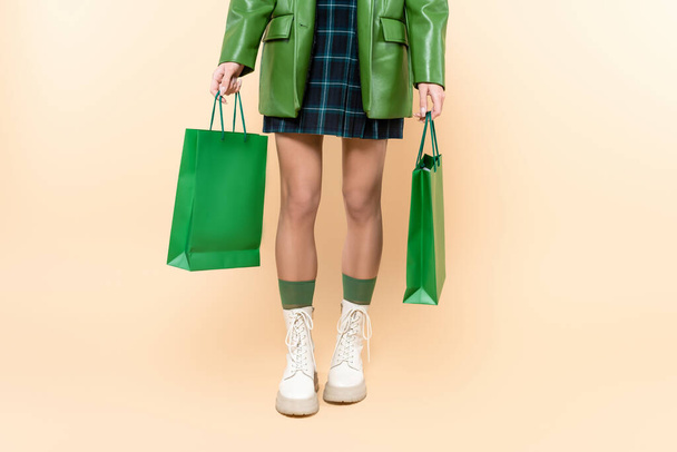 cropped view of woman in plaid skirt and white lace-up boots holding shopping bags on beige - Foto, Imagem