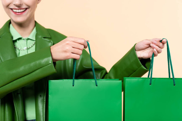 cropped view of smiling woman with green shopping bags isolated on beige - Foto, afbeelding