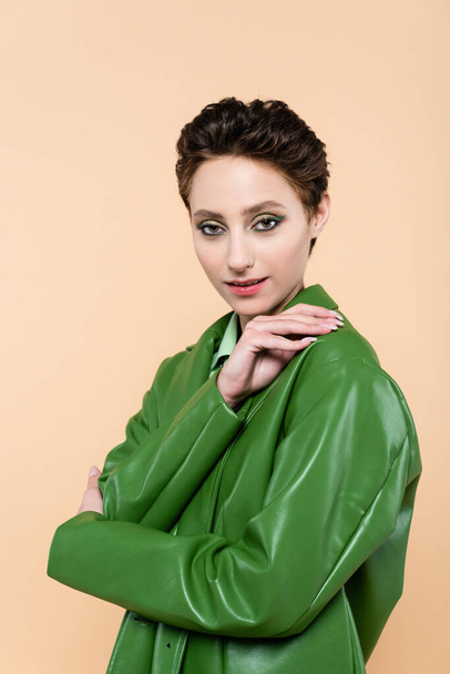 brunette woman with short hair, wearing green leather jacket, posing isolated on beige - Photo, Image