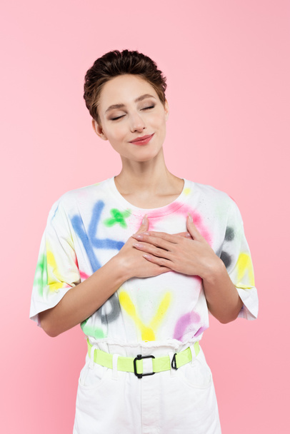 happy brunette woman with closed eyes holding hands on chest isolated on pink - Photo, Image