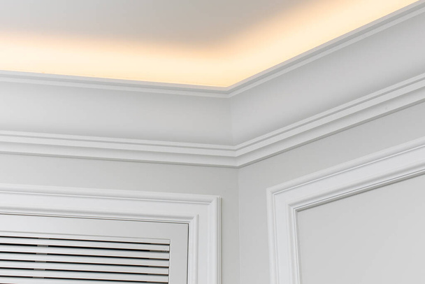 Close-up detail of renovation in modern interior. Angular ceiling skirting made of classic white moldings with built-in LED ceiling lighting. - Photo, Image