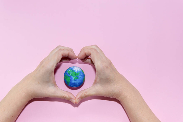 Green Energy, Renewable and Sustainable Resources. Environmental and Ecology Care Concept. Hands doing heart gesture on earth on pastel pink background. - Photo, Image
