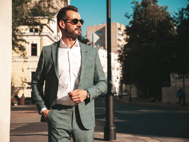 Portrait of handsome confident stylish hipster lambersexual model.Sexy modern man dressed in elegant suit. Fashion male posing in the street background in Europe city at sunset. In sunglasses - Foto, Bild
