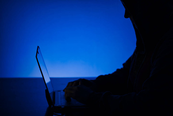 A closeup of the silhouette of a person in a hood working on a computer - hacking concept - Fotoğraf, Görsel