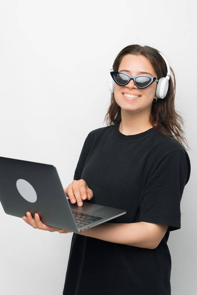 Portrait of young woman in cool sunglasses carrying laptop and using headphones, gadgets concept - Fotoğraf, Görsel