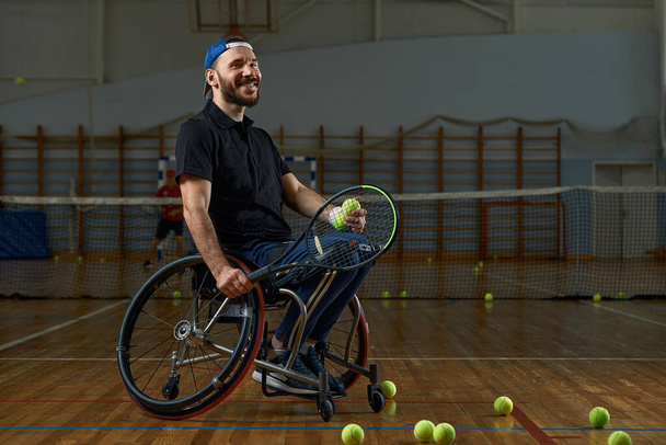 Młody mężczyzna na wózku inwalidzkim gra w tenisa na korcie - Zdjęcie, obraz